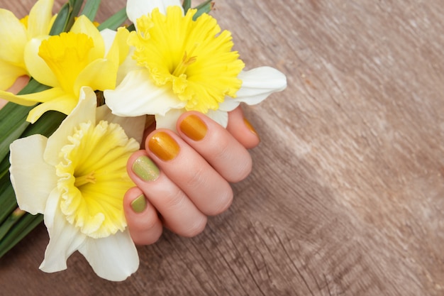 黄色のネイルデザイン 水仙の花を保持しているキラキラのマニキュアで女性の手 無料の写真