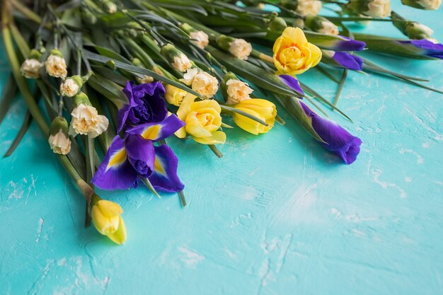 青い背景に分離されたラインフラワーアレンジメントの黄色い水仙の花と紫色の菖蒲 美しい春の花幸せな母の日 コピースペース プレミアム写真