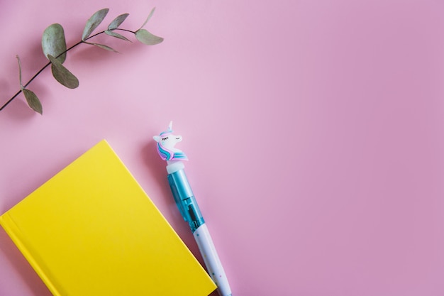 Yellow notebook for notes, funny unicorn pen and green eucalyptus leaves on pink pastel background. flat lay. top view. copy space Premium Photo