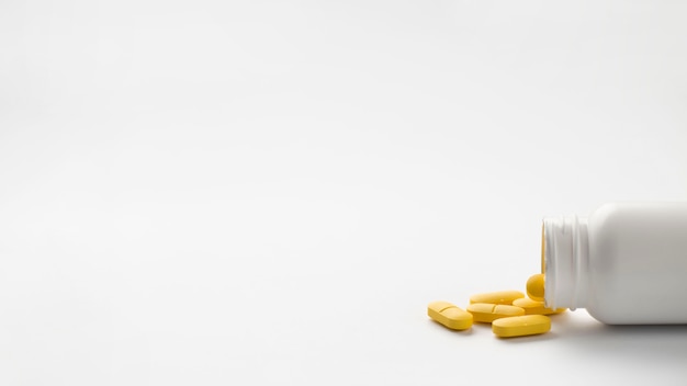 Free Photo Yellow pills spilled from bottle isolated over white 