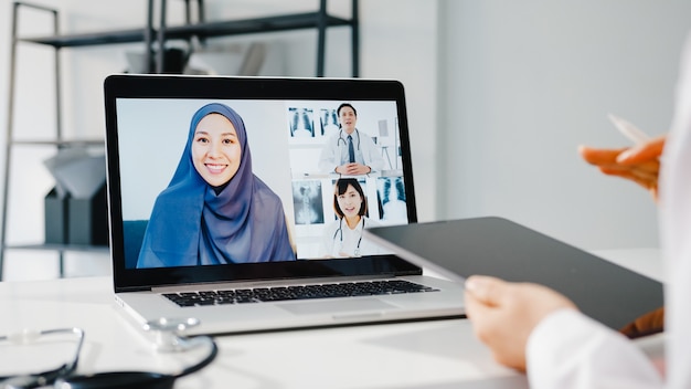 Young asia female doctor in white medical uniform with stethoscope using computer laptop talking video conference call Free Photo