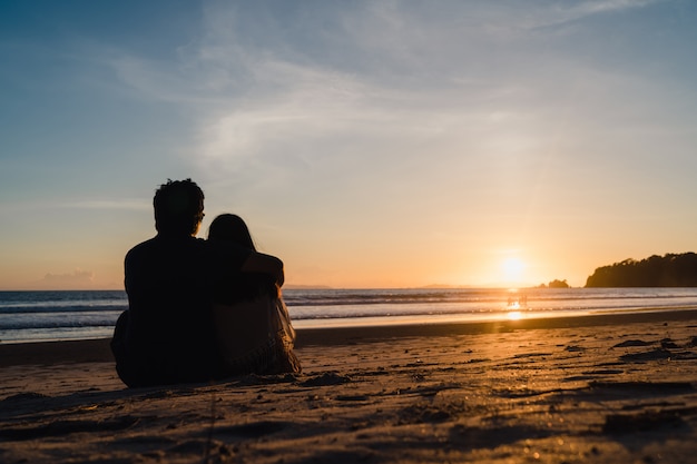 Young asian couple watching sunset near beach, sweet couple happy relax enjoy love and romantic moment Free Photo