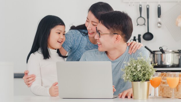 Young asian family enjoy using laptop together at home. lifestyle young husband, wife, and daughter happy hug and play after have breakfast in modern kitchen at house in the morning . Free Photo