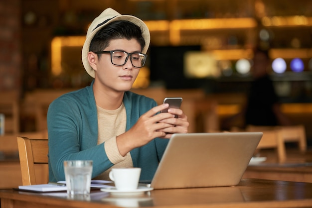 Young asian hipster man sitting in cafe with laptop and using smartphone Free Photo