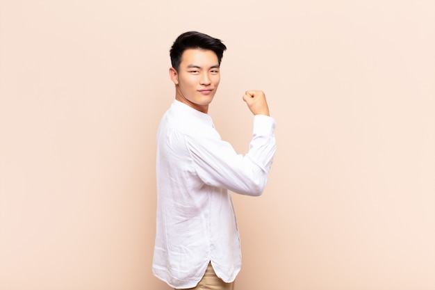 Premium Photo | Young asian man feeling happy, satisfied and powerful,  flexing fit and muscular biceps, looking strong after the gym over color  wall