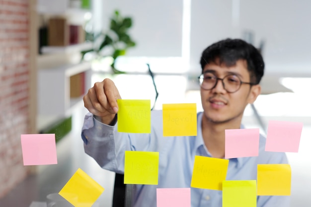 Premium Photo Young Asian Man Reading Sticky Note On Glass Wall At Office Business Brainstorming Creative Ideas Office Lifestyle Success In Business
