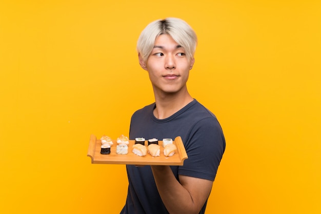 Young asian man with sushi over isolated yellow laughing Premium Photo