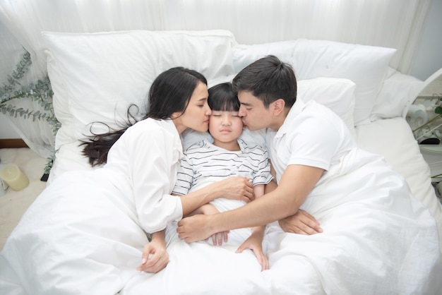 若いアジアの母 父と少年がベッドで寝ている ママとパパが息子の頬にキス 上からの眺め プレミアム写真