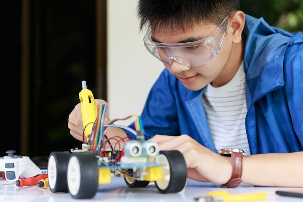 Young asian teen plugging energy and signal cable to sensor chip of toy car workshop. Premium Photo
