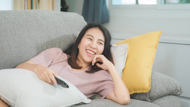 Young asian teenager woman watching tv at home, female feeling happy lying on sofa in living room. lifestyle woman relax in morning at home concept. Free Photo