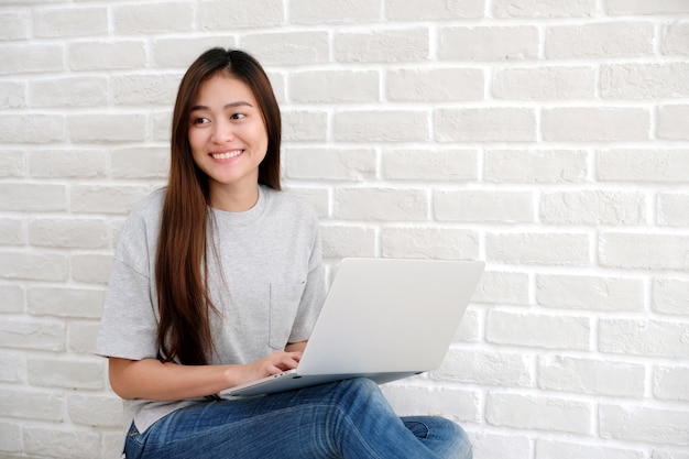 Young asian woman using laptop computer sitting in front of white ...