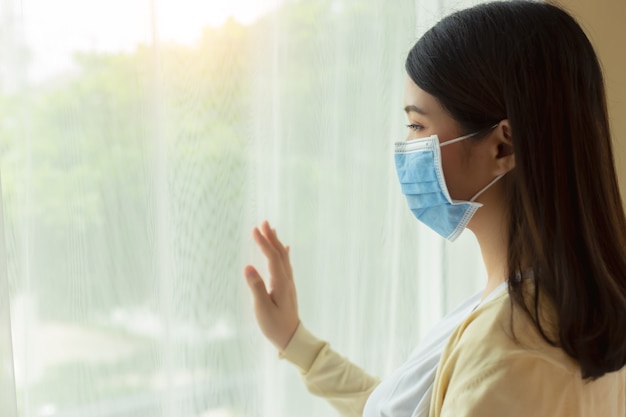 Premium Photo | Young asian woman wear protective face mask stay at home,  looking through window. covid 19, coronavirus concept