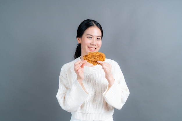 幸せそうな顔でセーターを着て、フライドチキンを食べることを楽しむ若いアジアの女性 プレミアム写真