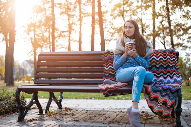 Young and attractive girl sitting on a bench in autumn park and drinking coffee Premium Photo