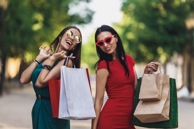 Premium Photo Young Attractive Girls With Shopping Bags In The Summer City Beautiful Women In Sunglasses Looking At Camera And Smiling Positive Emotions And Shopping Day Concept