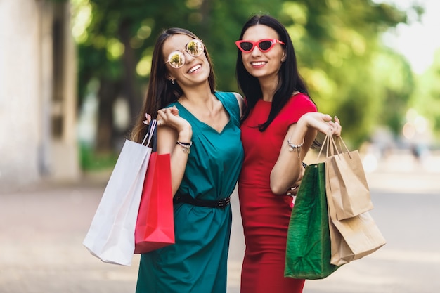 Premium Photo Young Attractive Girls With Shopping Bags In The Summer City Beautiful Women In Sunglasses And Smiling Positive Emotions And Shopping Day Concept