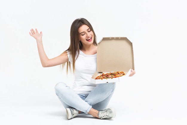 Young attractive woman eating a piece of delicious pizza. she a t-shirt, jeans and sneakers sitting 