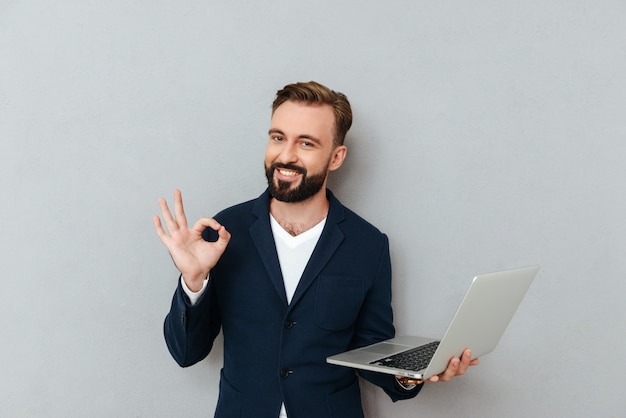 Young bearded man in suit looking camera while holding laptop computer isolated Free Photo