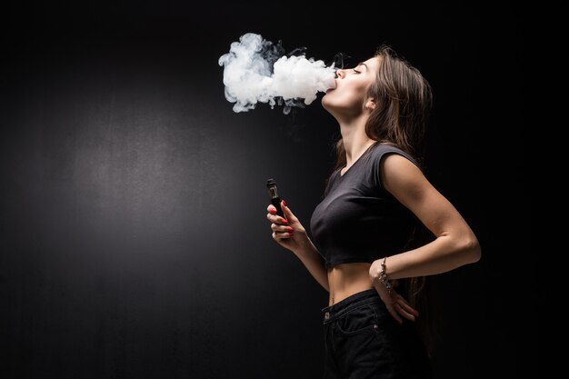 젊은 아름 다운 갈색 머리 여자 흡연 검은 벽에 연기와 전자 담배 Vaping 무료 사진 5693