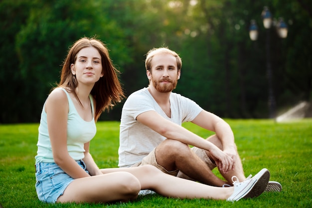 Free Photo | Young beautiful couple smiling, sitting on grass in park.