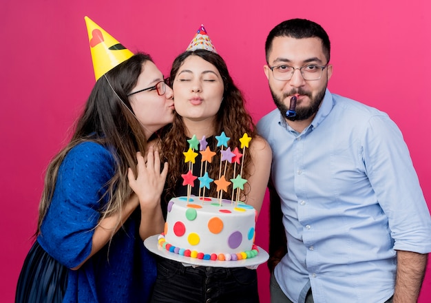 ピンクの上の彼女の友人の誕生日パーティーのコンセプトとバースデーケーキを保持している巻き毛の若い美しい女性 無料の写真