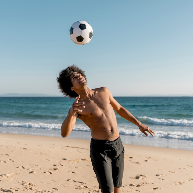 ビーチでサッカーボールをプレーする若い黒人選手 無料の写真