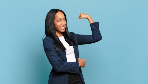 Young black woman feeling happy, satisfied and powerful, flexing fit and muscular biceps, looking strong after the gym. business concept Premium Photo