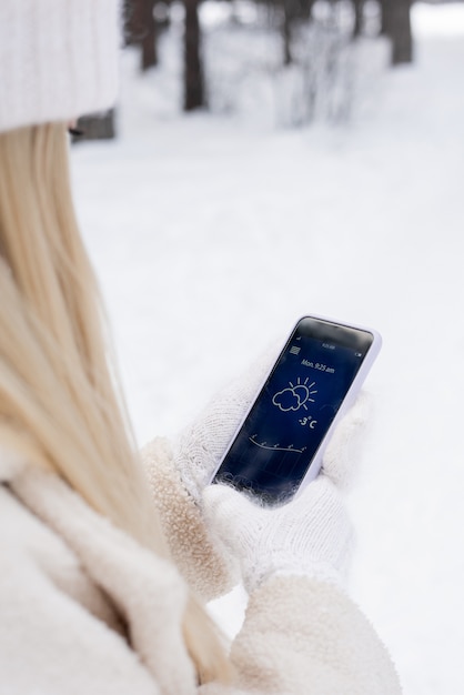 Premium Photo Young Blond Woman In White Fluffy Knitted Mittens Looking For Temperature Outside In Smartphone While Chilling In Park