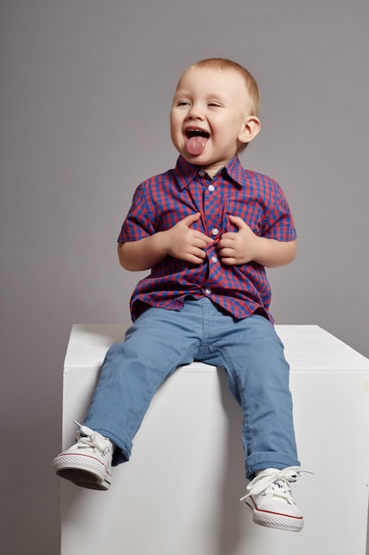 Young boy child smiling sitting on white cube Premium Photo