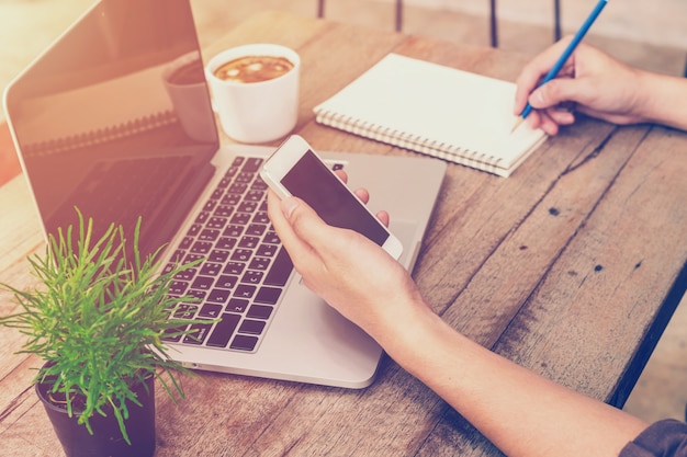 Young business man hand holding phone and writing and using laptop ...