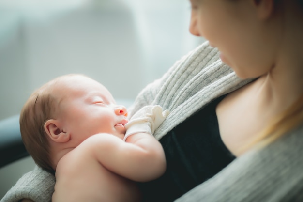 手に彼女の小さな眠っている生まれたばかりの赤ちゃんを保持している若い白人の母親 プレミアム写真