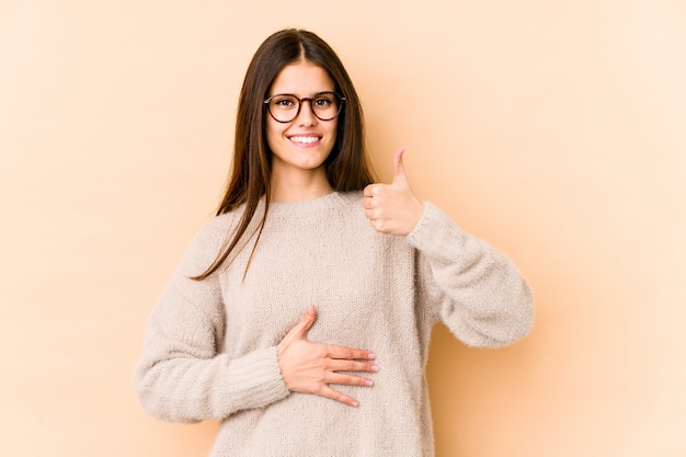 Young caucasian woman on beige wall touches tummy, smiles gently Premium Photo