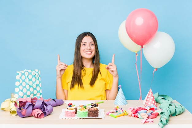 Young caucasian woman organizing a birthday indicates with both fore fingers up showing a blank space. Premium Photo
