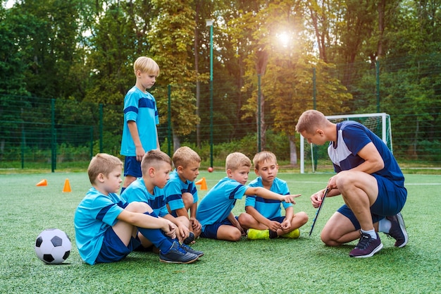 若いコーチがサッカーのフィールドでプレーする戦略を小さな子供たちに教える プレミアム写真