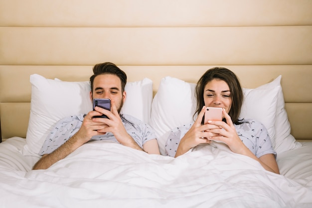Free Photo | Young couple in bed using smartphones