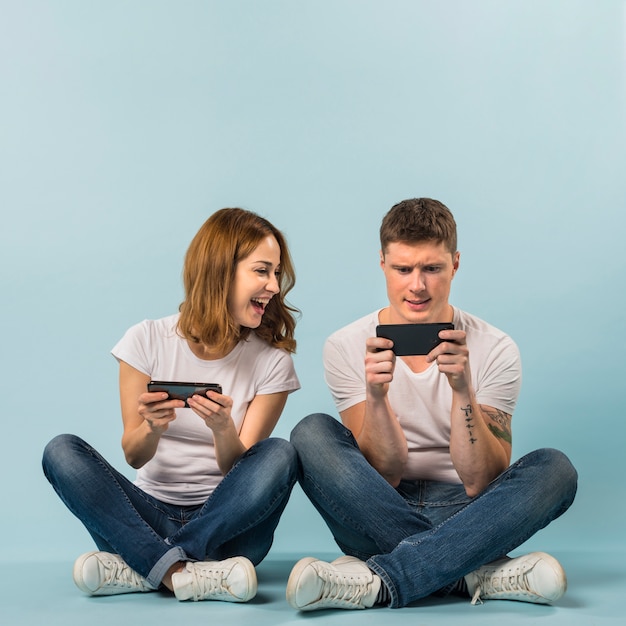 青い背景に携帯電話でビデオゲームを楽しむ若いカップル プレミアム写真
