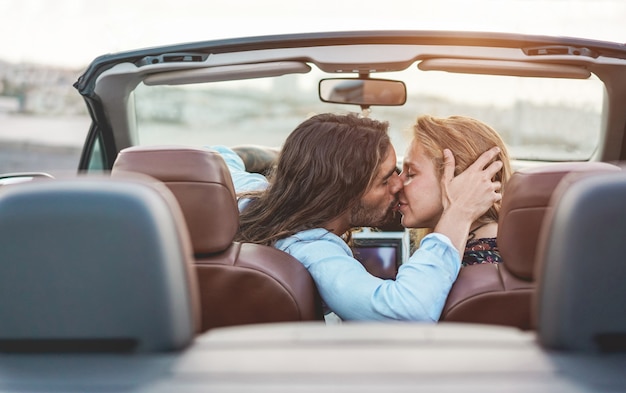 背景のパノラマビューとコンバーチブル車の中でキスする若いカップル ロマンチックなデートに優しい瞬間を持っている人 愛 旅行 関係の概念 顔に焦点を当てる プレミアム写真