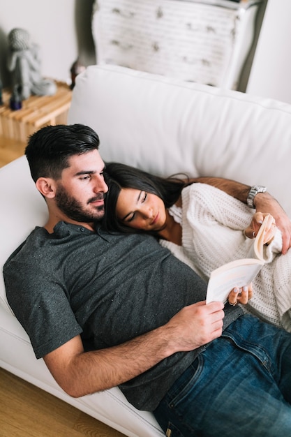 Free Photo | Young couple lying on white sofa reading book