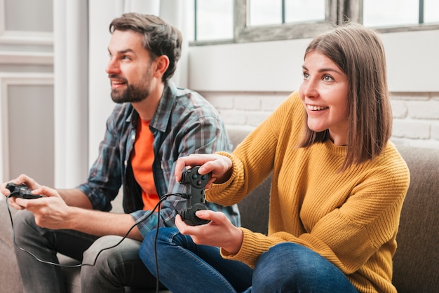 Young couple sitting on sofa enjoying playing the video game Free Photo