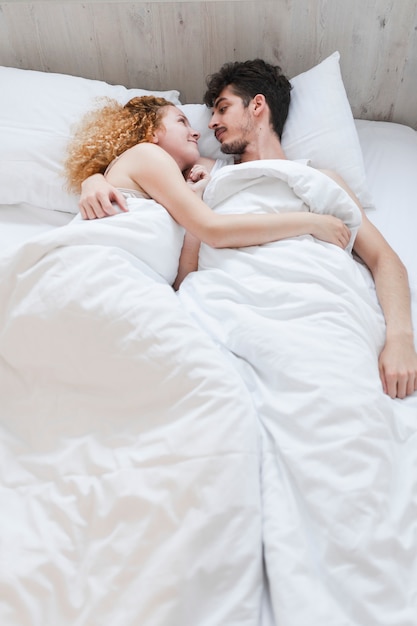 Free Photo Young Couple Wrapped In Blanket Lying On Bed