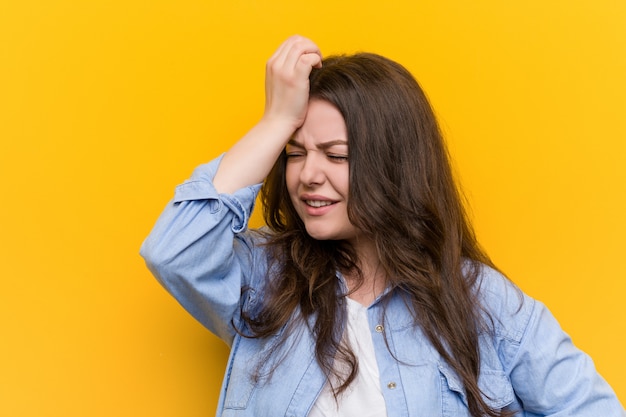 Young curvy plus size woman forgetting something, slapping forehead with palm and closing eyes. Premium Photo