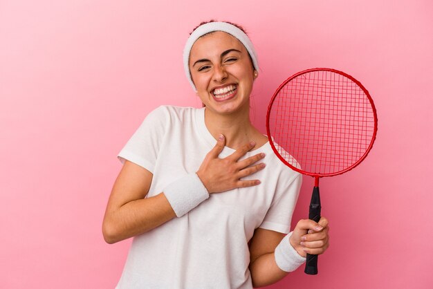 ピンクの背景に分離されたバドミントンラケットを保持している若いかわいい金髪の白人女性は 胸に手を置いて大声で笑います プレミアム写真