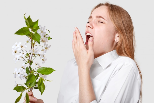 春の花にアレルギーがある若いかわいい女性 くしゃみ 口を大きく開いたままにしている 白のポーズ 臭いが好きではない 人 病気 アレルギーのコンセプト プレミアム写真