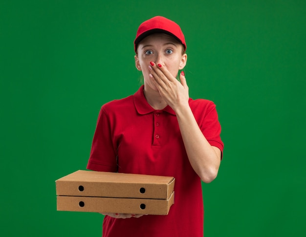 Free Photo Young Delivery Girl In Red Uniform And Cap Holding Pizza Boxes Being Shocked 5254