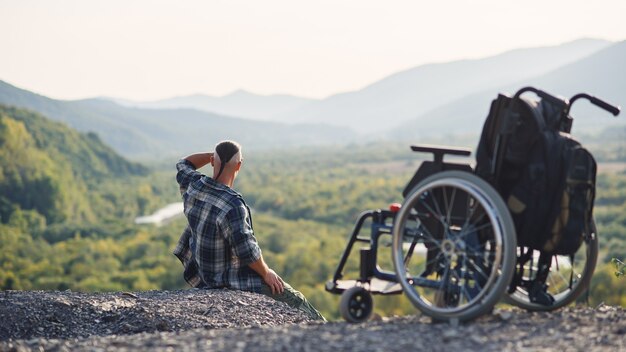 Premium Photo | Young man sitting on the mountain top near wheelchair and enjoying fresh air and nature beauty. enjoying life.