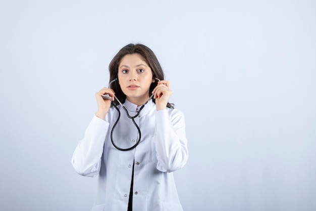 聴診器を使用して白い壁の脈拍をチェックする若い女性医師 プレミアム写真