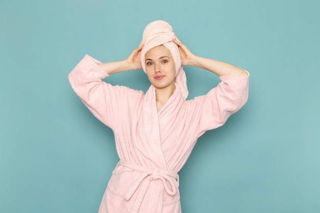 Young female in pink bathrobe after shower smiling and posing on blue Free Photo