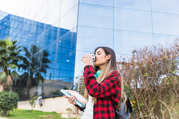 Young female student holding books in hand drinking the coffee | Free Photo