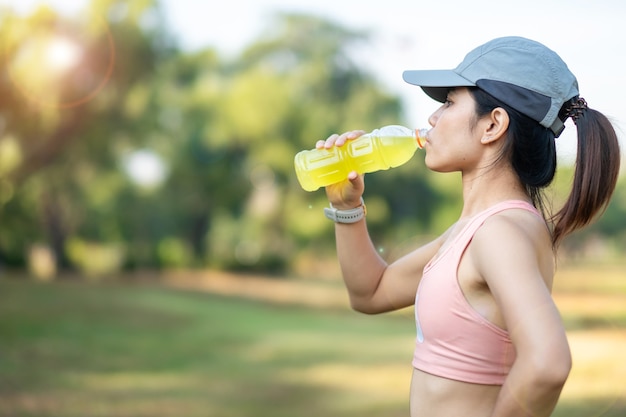 Premium Photo | Young fitness woman drinking energy water during stretching  muscle in the park outdoor, asian athlete running and exercise in morning.  sport and wellness concept