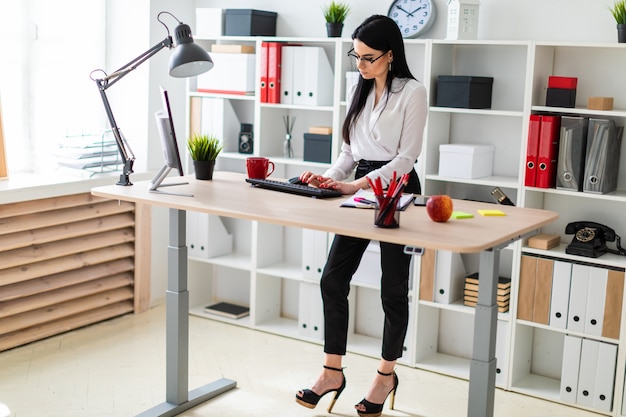 A young girl is standing near the table and typing text on the keyboard. next to the girl lie documents and a marker. Premium Photo